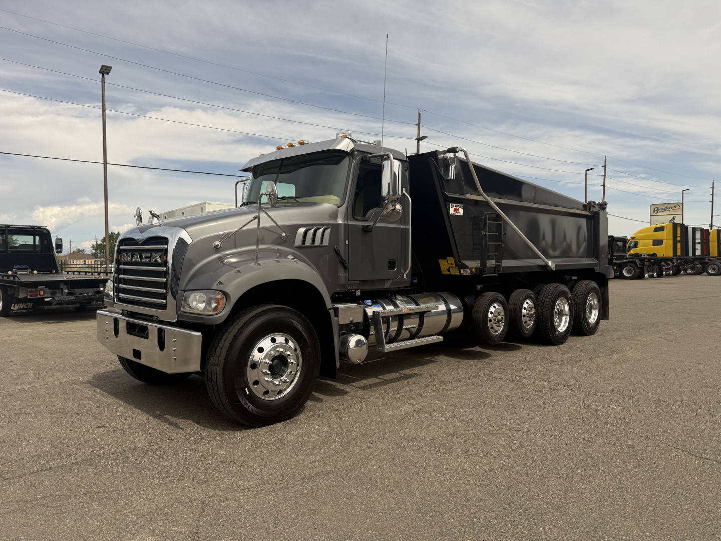 Dump truck in a parking lot showing Mack GR64F dump truck with gray cab and black dump bed.