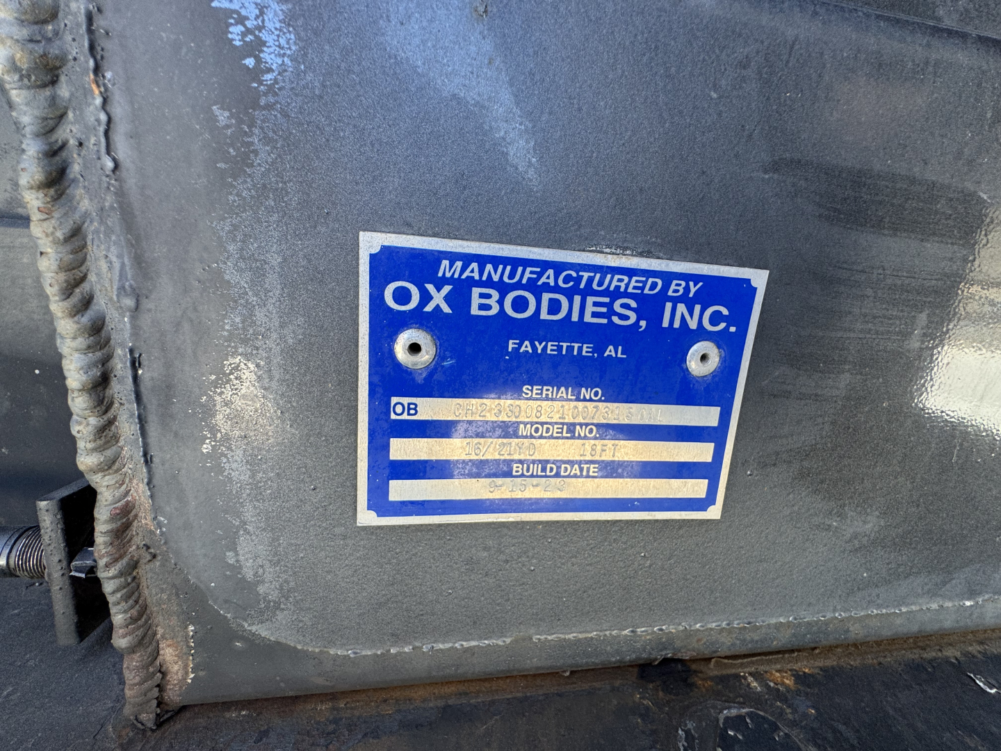 Label plate on metal surface reading MANUFACTURED BY OX BODIES, INC. FAYETTE, AL with fields SERIAL NO., MODEL NO., BUILD DATE visible.