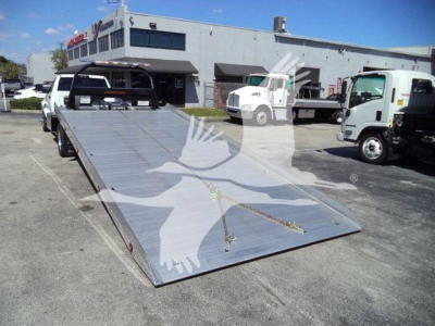 Ram 5500 rollback truck with a long metal loading ramp extended in the foreground.
