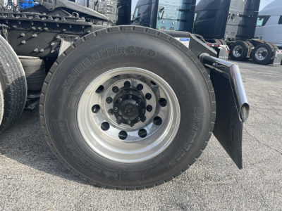 Volvo VNL64T860 front wheel close-up showing AlHill... wait no. Showing 22.5 inch Michelin (?) tire with wheel, fender mud flap, and trailer tractor chassis. Visible text on tire reads 'ALLI...'.