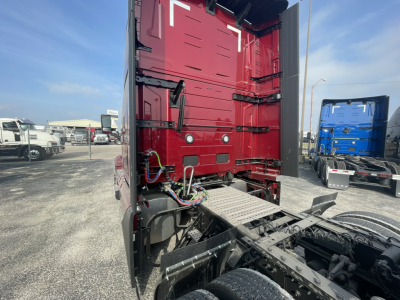 Volvo engine bay showing rear of cab and connected wiring harnesses for tractor truck with red sleeper, view from cab rear with chassis and fifth wheel area.