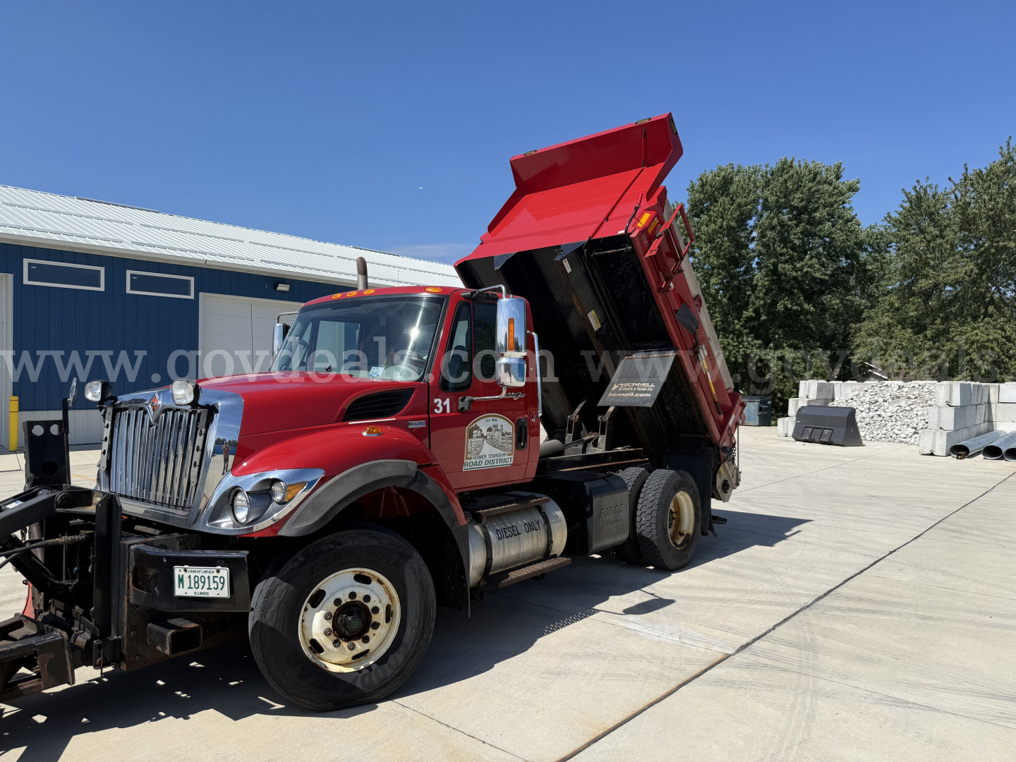 Dump truck in a lot with a red International 7400 dump bed raised. Visible text on cab door and license plate area.