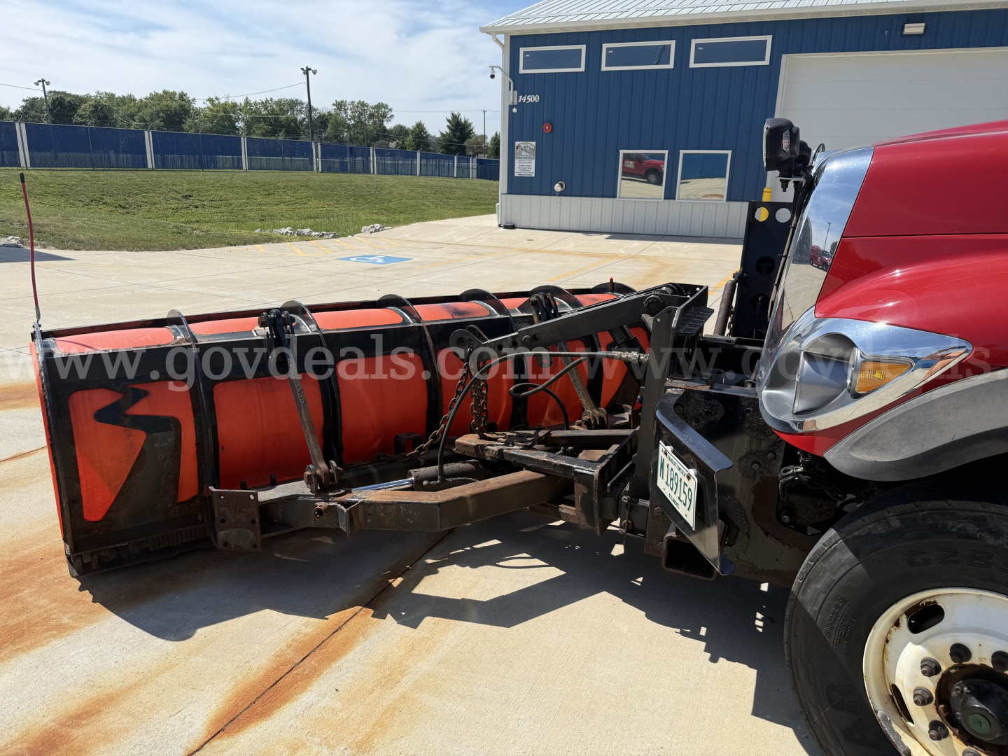 Truck front half with red International 7400 snow plow attachment in service bay, hydraulic hoses, and plow blade visible.