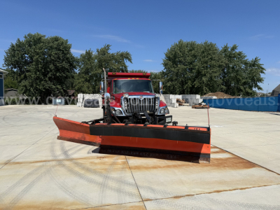 Front view of an International 7400 dump truck with a large orange snow plow blade attached in a paved lot.