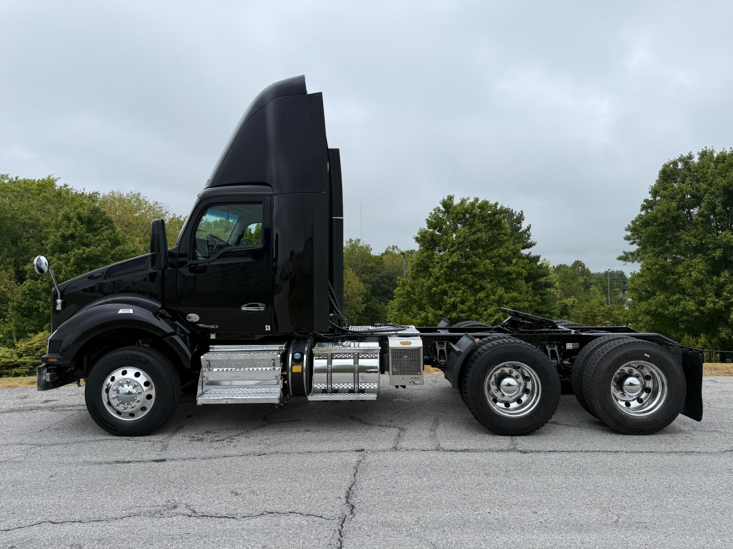 Kenworth T880 2020 conventional day cab side profile showing diesel exhaust stack, chrome fuel tanks, and dual rear axles against an overcast sky.