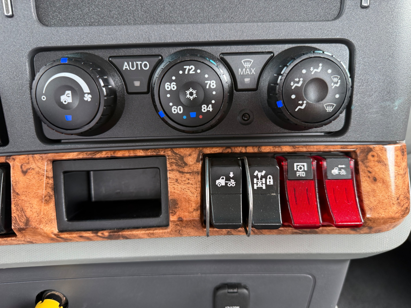 Dashboard controls of a 2020 Kenworth T880 showing climate knobs, auxiliary switches, and wood-grain panel with two red toggle switches.