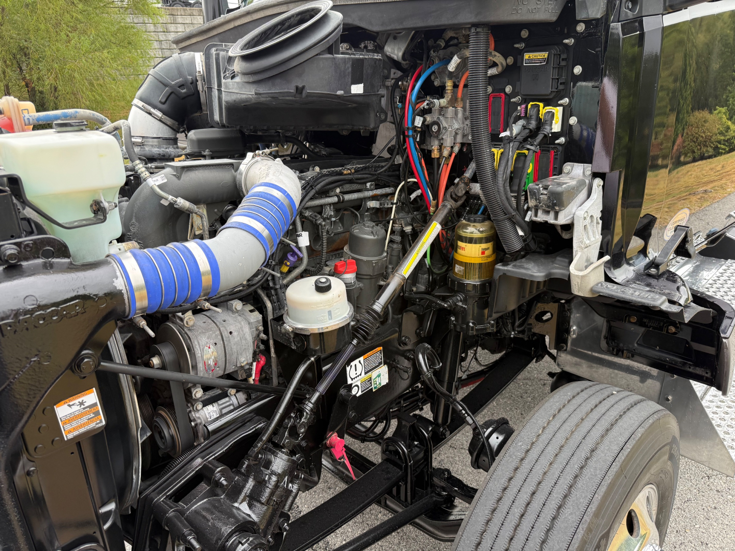 Kenworth T880 engine bay showing coolant reservoir, turbo intake, hoses, wiring, and engine components with blue silicone intake boot.