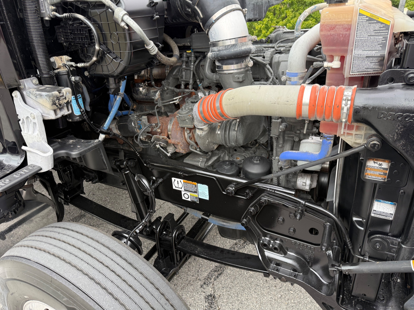 Kenworth T880 engine bay showing air intake, hoses, and coolant reservoir with orange and white hose in view.