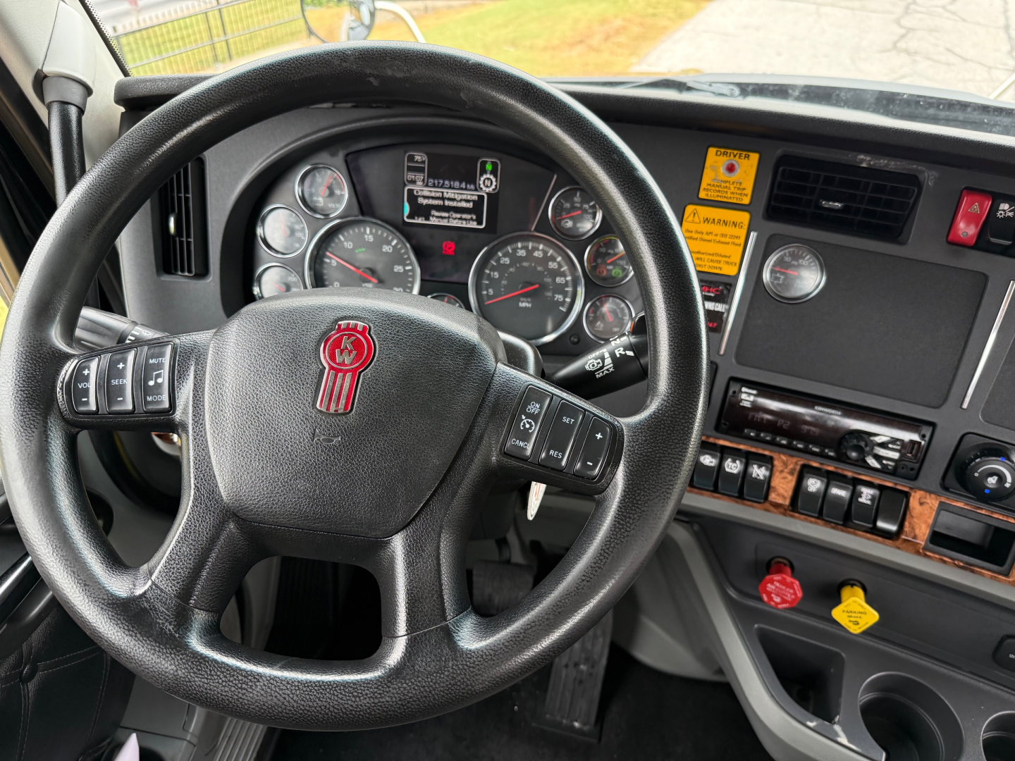 Kenworth T880 cab interior showing steering wheel with Kenworth emblem, instrument cluster, dashboard switches, and mounted display panel.