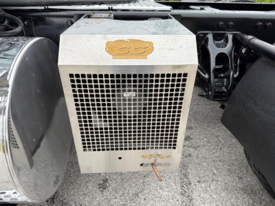 Kenworth T880 under-hood component showing a rectangular metal cooling unit with a mesh grille and a small emblem sticker on top.