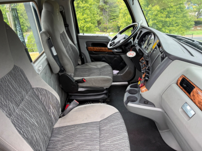 Kenworth T880 cab interior showing driver seat and passenger seat, steering wheel, dashboard with woodgrain accents, center console, and gear shifter.
