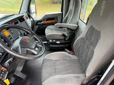 Kenworth T880 truck interior showing steering wheel, driver seat, and dashboard with gray fabric seats and wood trim.