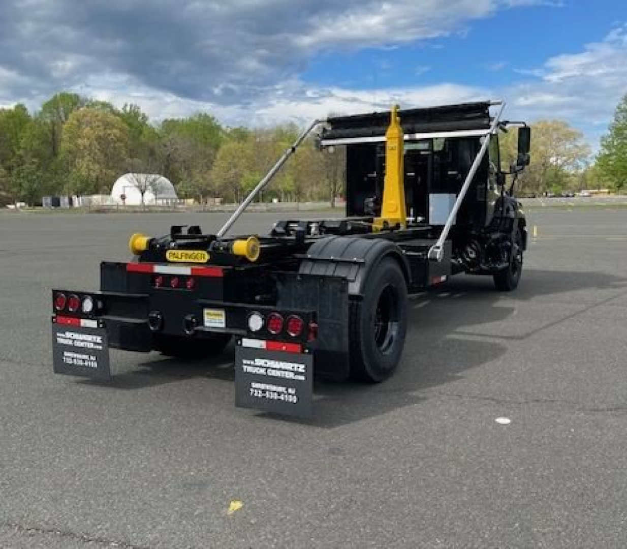 Hooklift truck rear view showing hydraulic lifting arm and chassis, Hino L7 with wheel blocks and rear mud flaps.