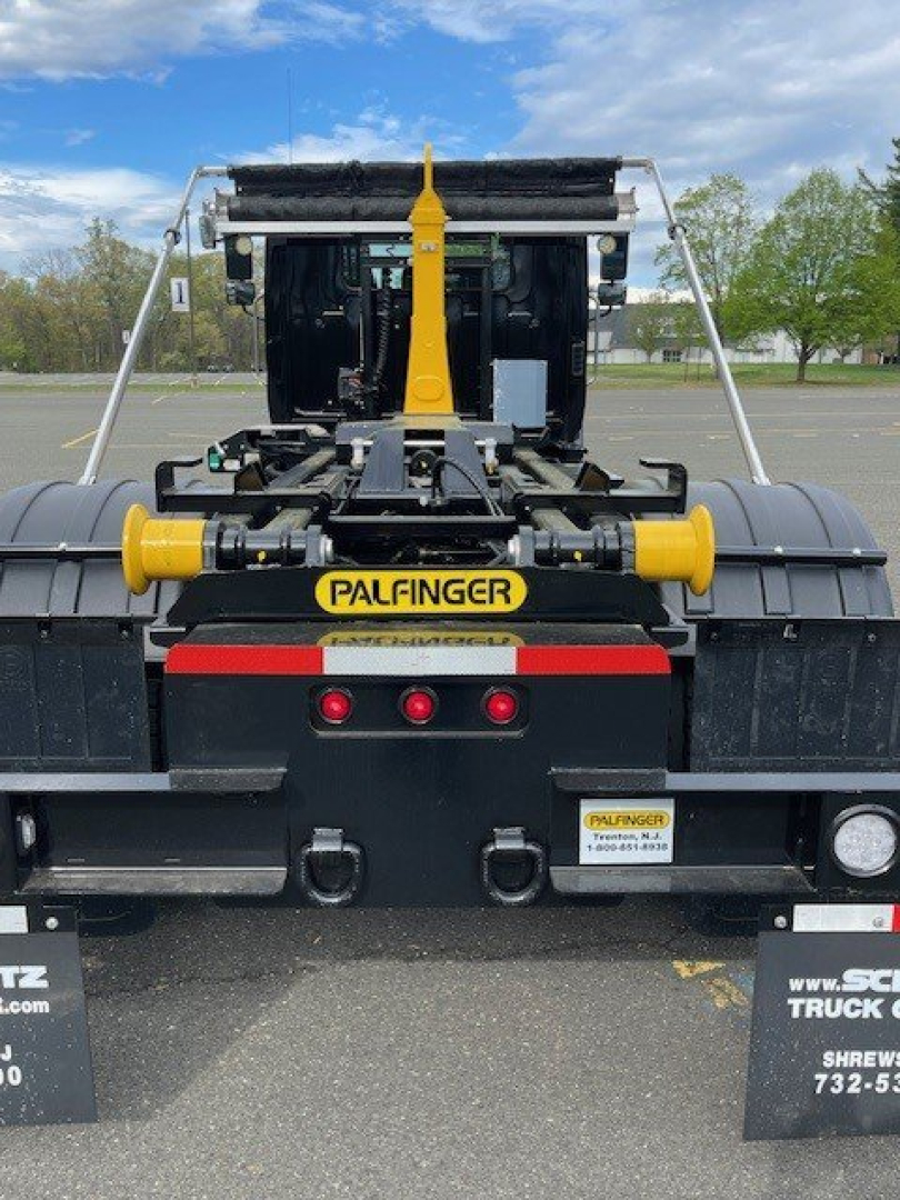 Truck rear view showing Palfinger hooklift assembly with yellow arms and black chassis, taillights and license plate area visible.