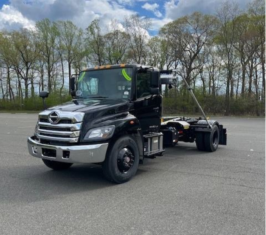 Black Hino L7 hooklift truck in a parking lot with a long wheelbase, front chrome grille, and extended chassis behind cab.