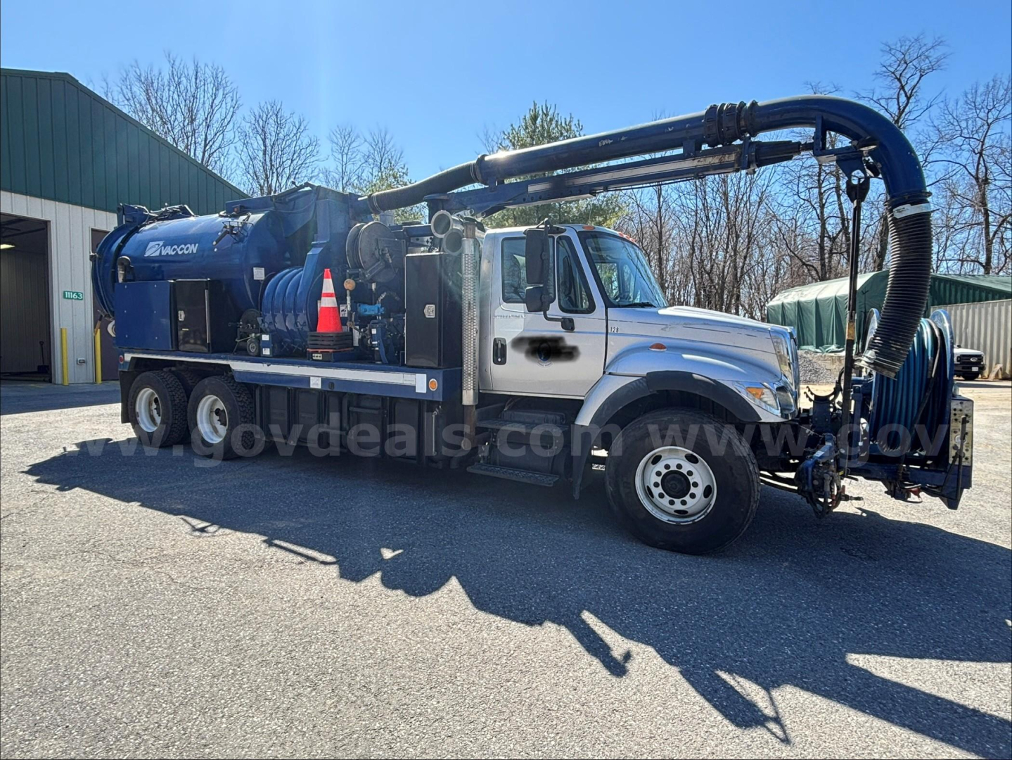 International 7500 vacuum truck with large blue crane and tank, side view showing hose reels and equipment.