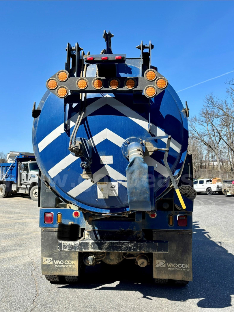 Back of vacuum truck showing circular rear tank with chevron pattern and hoses/pipe fittings.