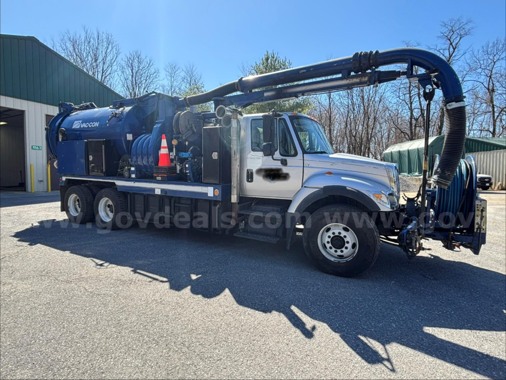 International 7500 vacuum truck with large blue crane and tank, side view showing hose reels and equipment.