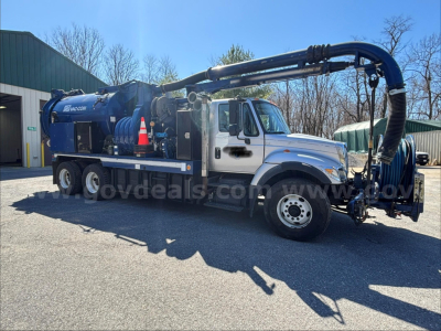 International 7500 vacuum truck with large blue crane and tank, side view showing hose reels and equipment.