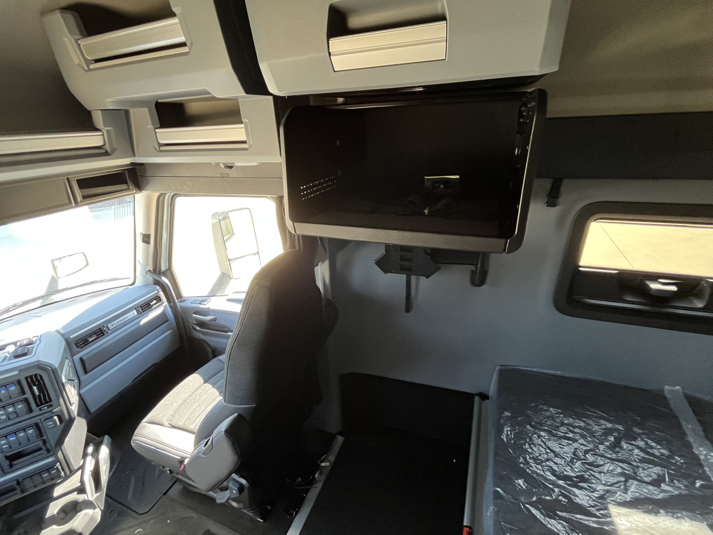 Mack PR64T76M tractor cab interior showing overhead bunk area and mounted monitor along with dashboard and driver seat.