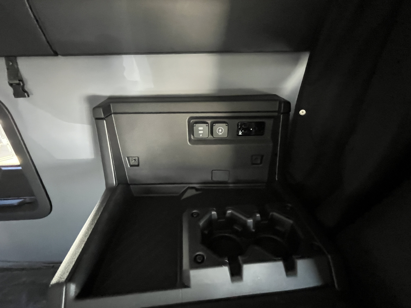 Pictured is a Mack truck cab interior area with a small black utility box mounted on the wall and a cup holder/storage recess below.