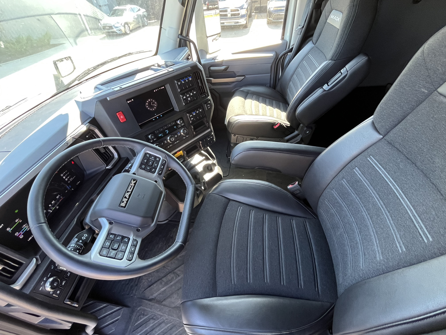 Mack PR64T76M truck cockpit interior showing steering wheel and driver seat with digital dashboard and center console.