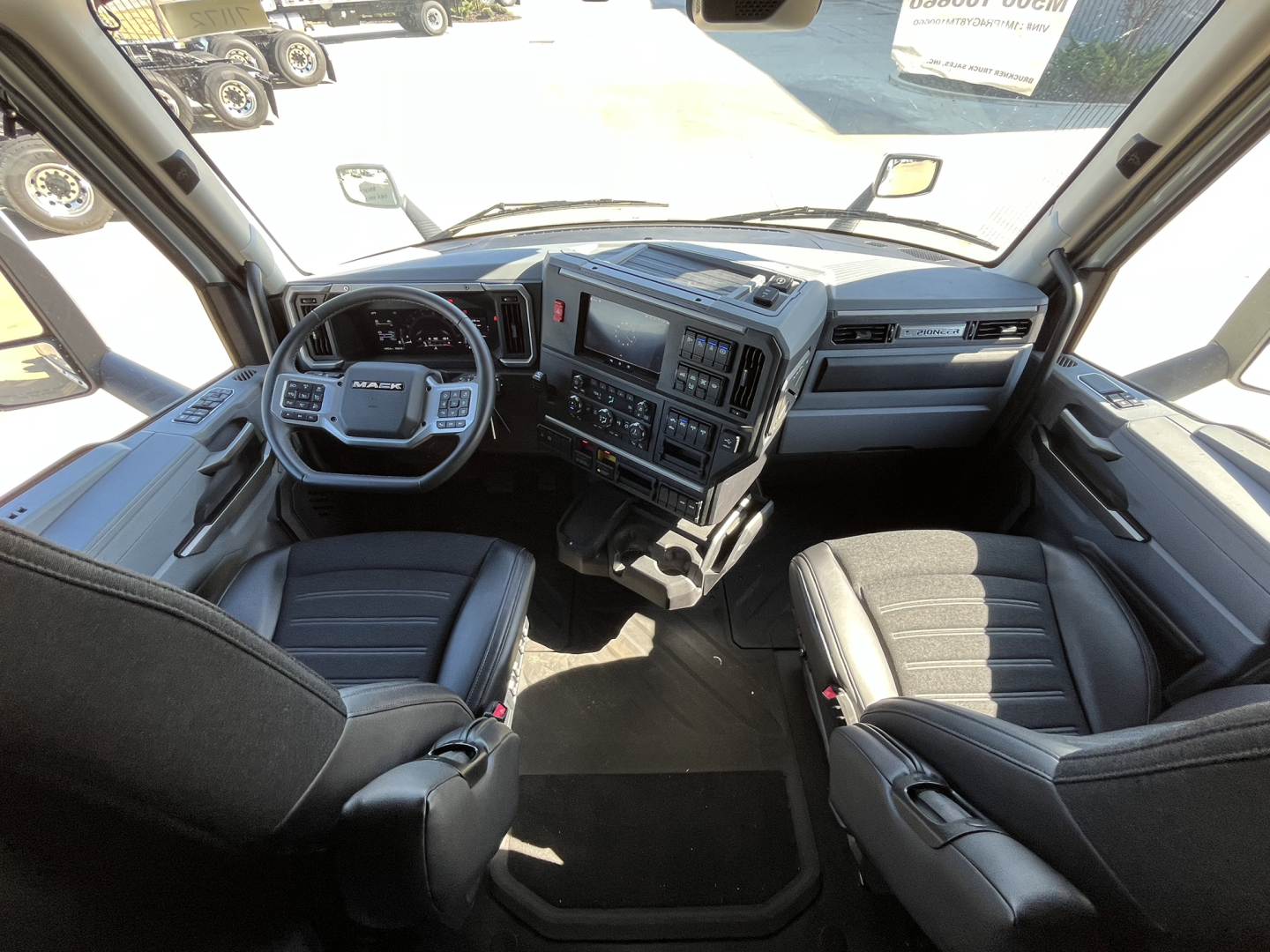 Mack PR64T76M truck interior showing driver and passenger seats, steering wheel, dashboard with controls and multimedia screen.