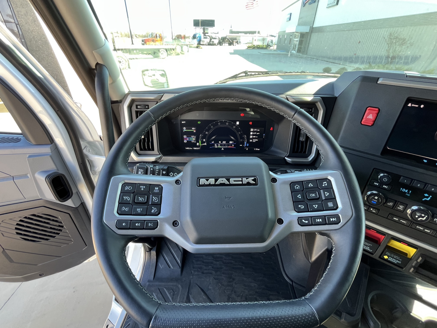 Mack truck interior view from driver seat showing steering wheel with Mack logo and digital instrument cluster.