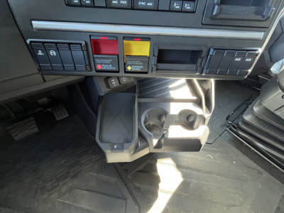 Cab interior of a 2026 Mack PR64T76M showing center console with colored warning buttons, cup holders, and floor area.