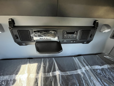 Interior cab view of a new Mack PR64T76M sleeper truck showing dashboard panel, storage, and plastic-wrapped seating.