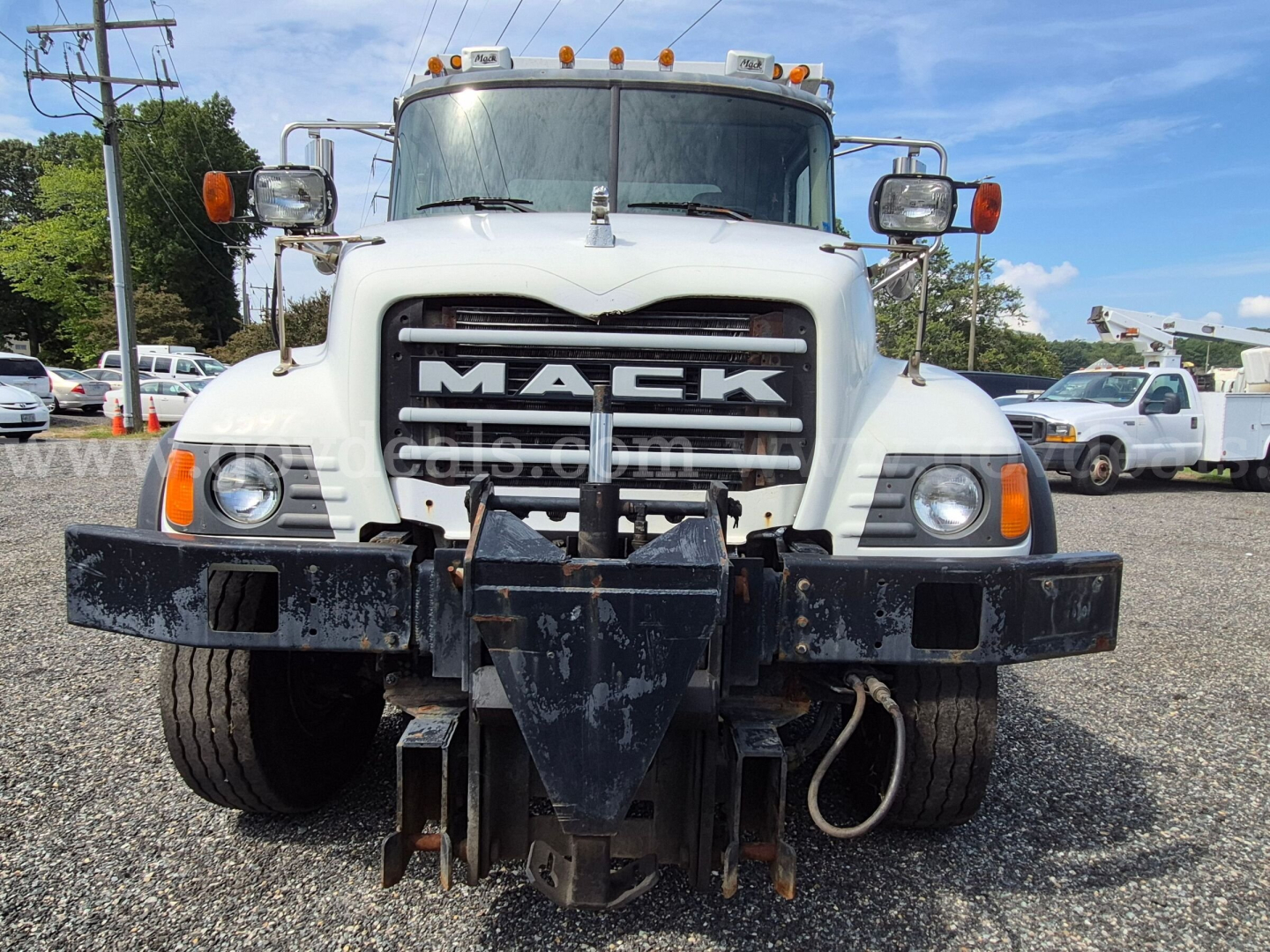 Mack CV713 front view showing large grille with MACK lettering, heavy front bumper with hitch, two round headlights, and orange marker lights.