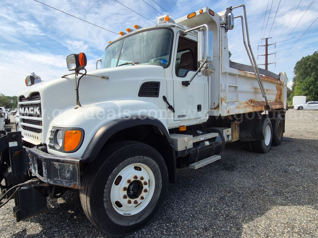 Mack CV713 dump truck viewed from front-left showing cab and dumping bed with orange warning lights on top.