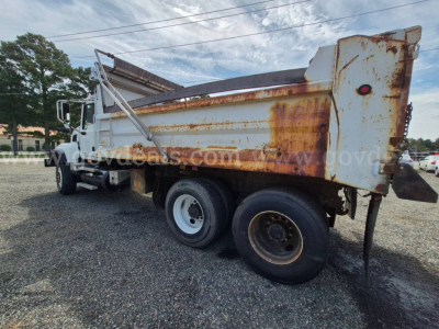 Dump truck showing rusted dump bed and rear wheels, white cab, side view of Mack CV713 with rust stains on tailgate.