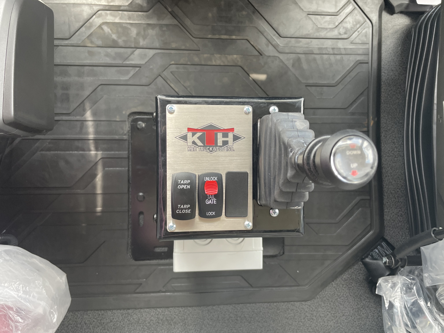 Volvo VHD64F300 truck interior view showing a control box with KD logo and switch labels 'TAMP OPEN', 'TAMP CLOSE', 'GATE LOCK', mounted on a textured floor mat.