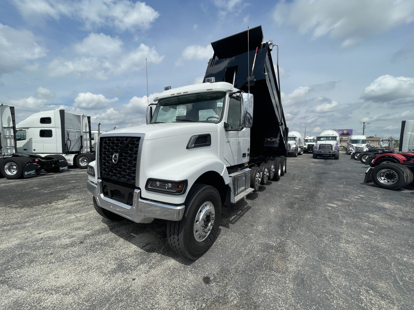 2026 Volvo VHD64F300 dump truck with a raised dump bed, frontal view, in a dealership lot with other trucks in the background.