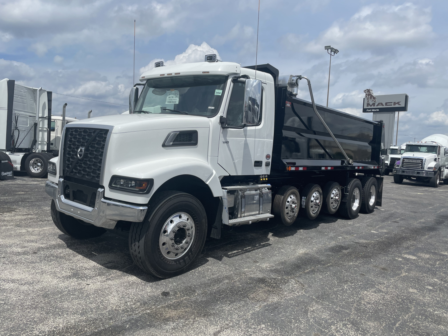 Dump truck in a dealership lot showing a white Volvo VHD64F300 cab and a black dump bed with multiple rear axles.
