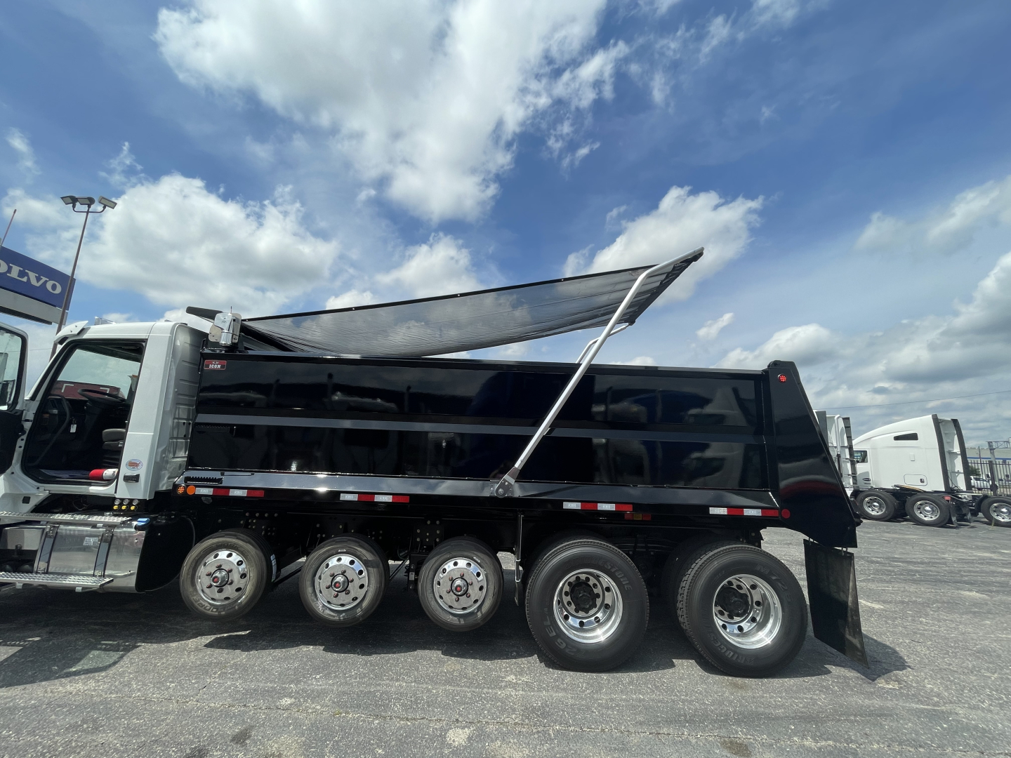 Volvo VHD64F300 dump truck side view showing multiple rear axles and dump bed, with windshield and cab visible.