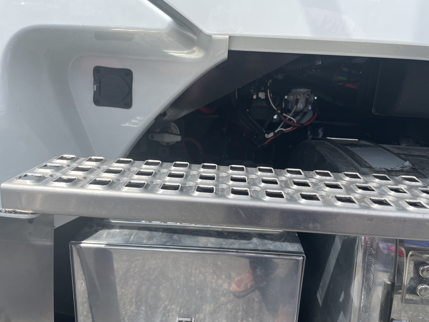 Truck engine bay area of a Volvo VHD64F300 showing a rectangular metal utility box and a perforated step/footboard with cables visible in background.