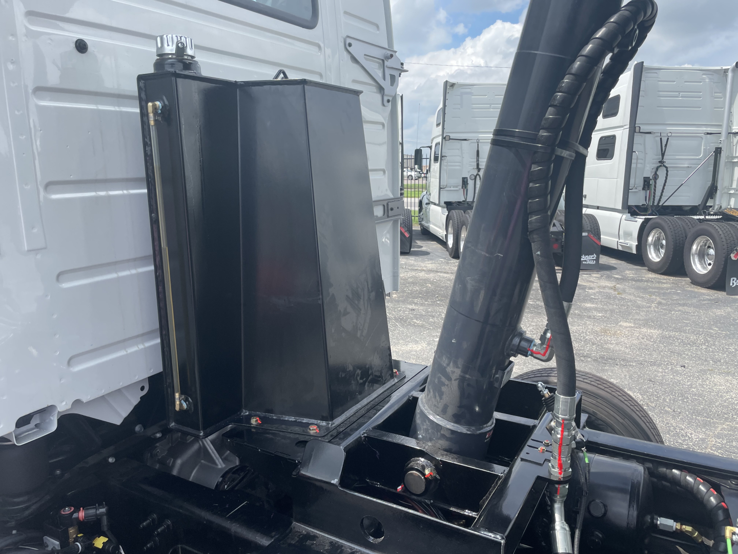 Volvo VHD64F300 truck engine bay area showing large black hydraulic reservoir mounted near cab and hose assembly.