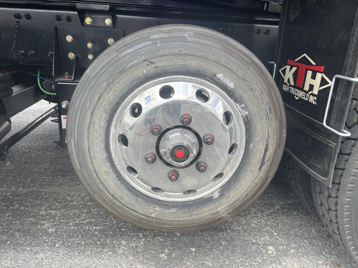 Volvo VHD64F300 dump truck wheel showing aluminum rim with red center nut and lug nuts, tire tread visible, chassis and part of hydraulic lines.