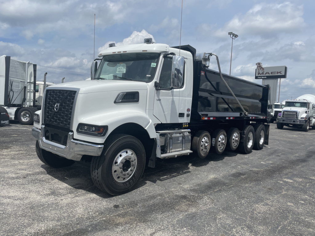 Dump truck in a dealership lot showing a white Volvo VHD64F300 cab and a black dump bed with multiple rear axles.