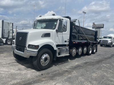 Dump truck in a dealership lot showing a white Volvo VHD64F300 cab and a black dump bed with multiple rear axles.