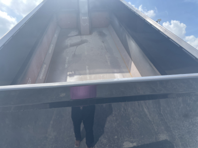 Dump truck bed interior with metal sidewalls and floor, viewed from tailgate opening; light reflections and shadowy area inside bed.