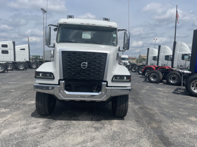 Front view of a new Volvo VHD64F300 dump truck with bold black grille and headlights, Volvo emblem on the grille, in a dealership lot.