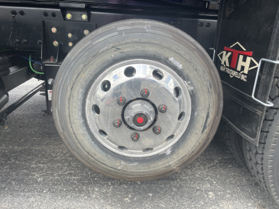 Volvo VHD64F300 dump truck wheel showing aluminum rim with red center nut and lug nuts, tire tread visible, chassis and part of hydraulic lines.