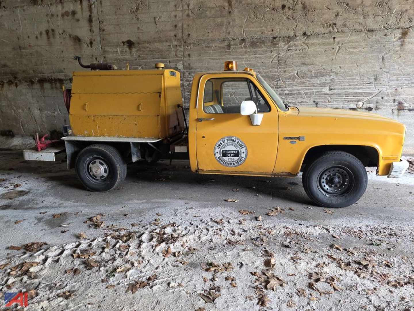 GMC C/K 2500 series pickup with yellow utility body and emblem on door, side view showing front cab and rear service unit with tank, in a garage.