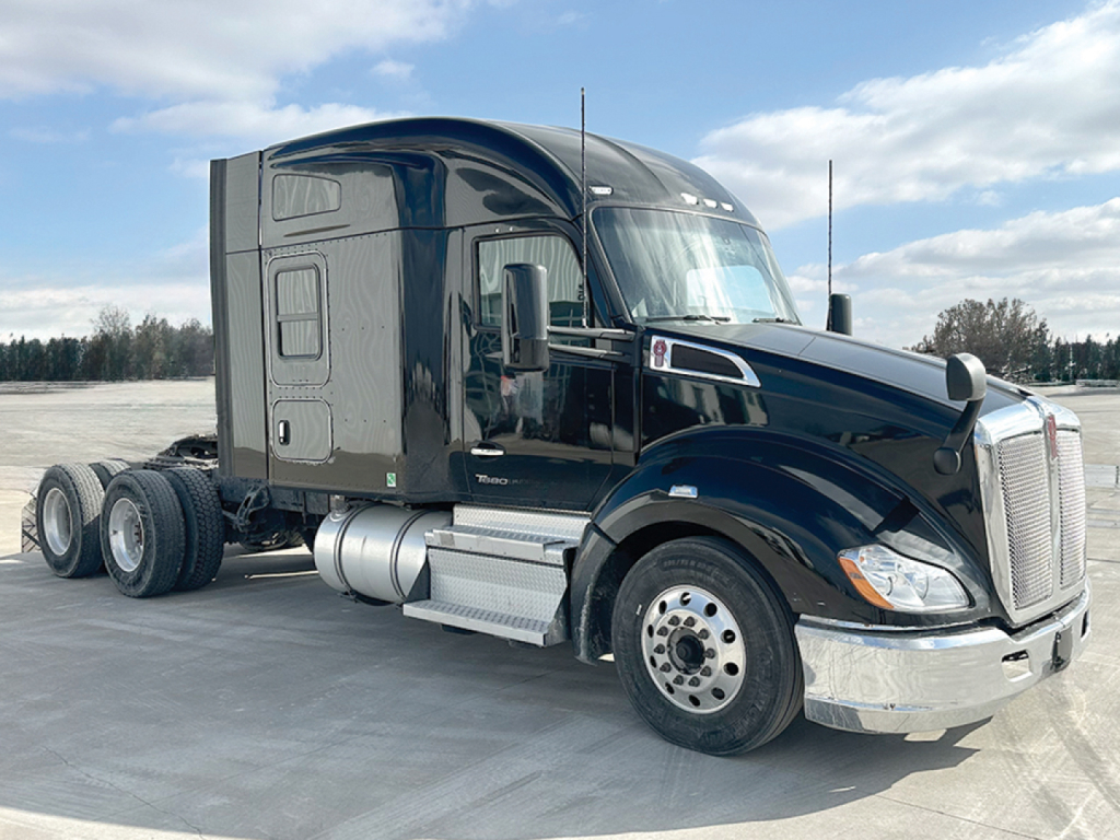 Kenworth T680 conventional sleeper truck in dark blue, side view showing tractor cab, chrome bumper, aluminum fuel tanks, dual rear axles, and large front grille.