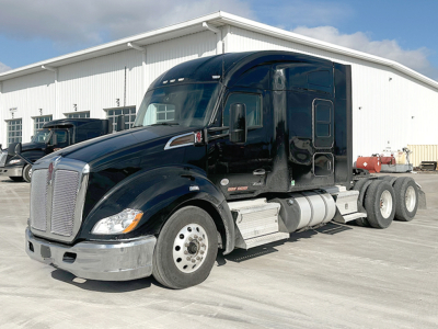 Kenworth T680 tractor-trailer in a lot, black cab, chrome bumper, six wheels visible, side steps and fuel tanks.