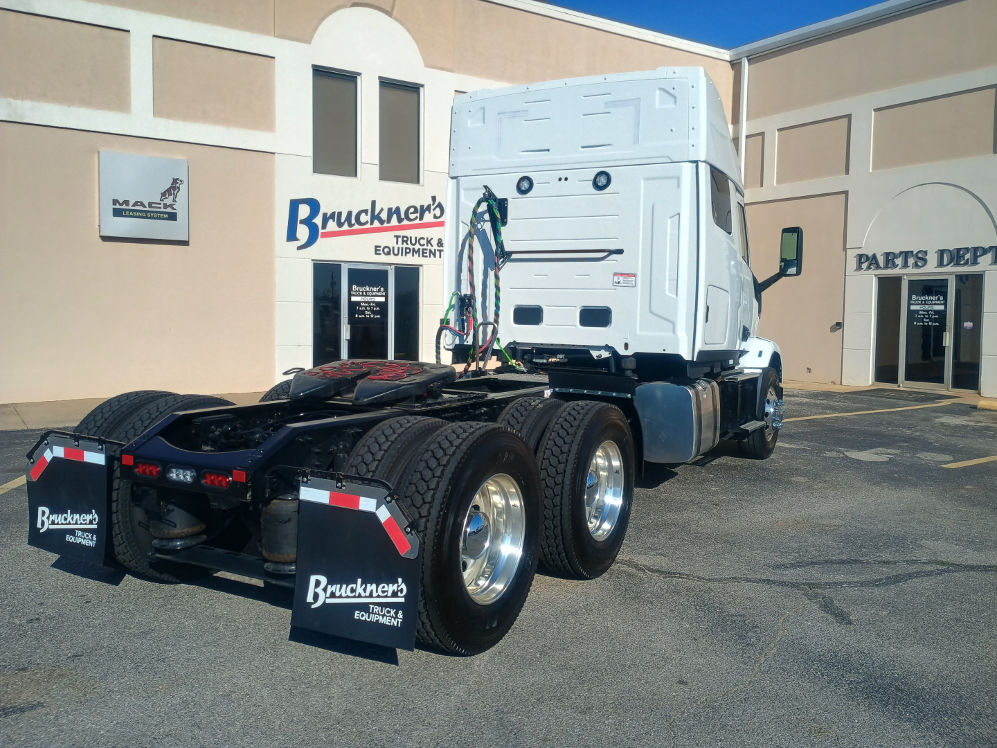 Truck chassis and cab of a 2027 Mack AN64T64 conventional sleeper, exposed rear dual-axle setup, white cab, at a dealership lot.