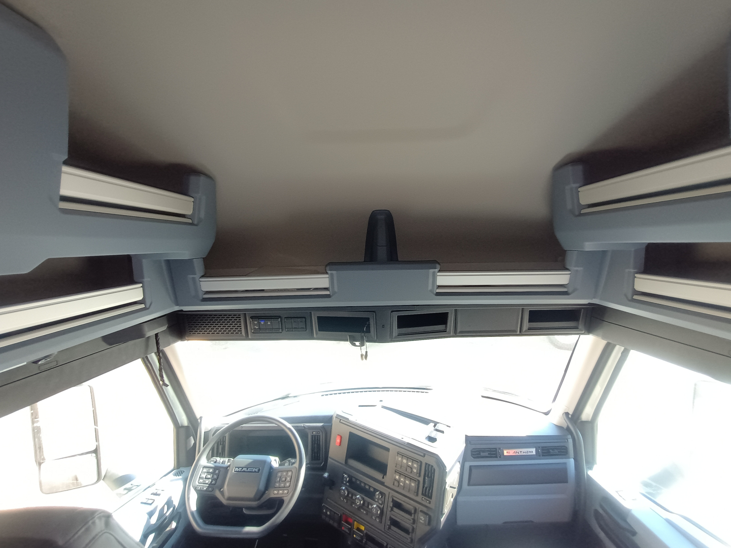 Truck cabin interior from front view; dashboard layout with steering wheel, center console, and overhead sleeper compartments visible.